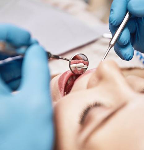 Close up of dentist examining a patient’s teeth with dental mirror