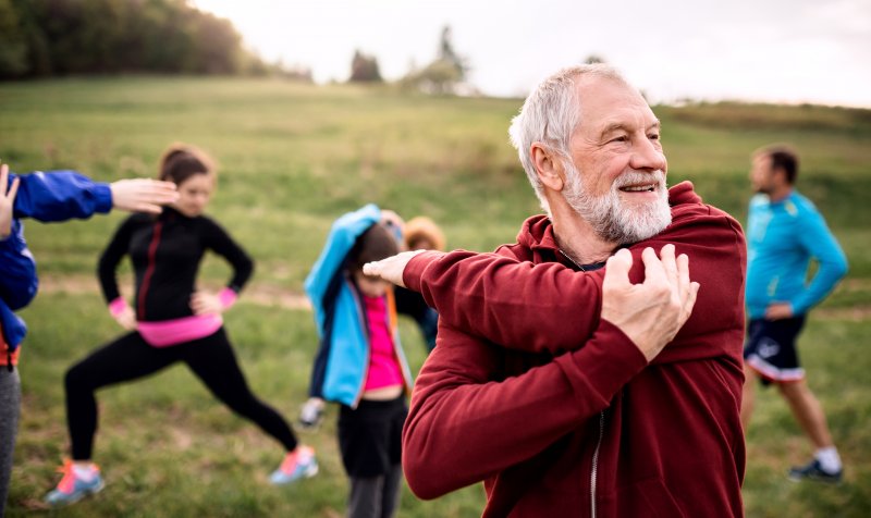 An older, smiling man exercising in nature alongside a group