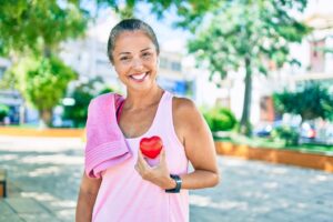Woman smiling and holding up red heart over her chest.